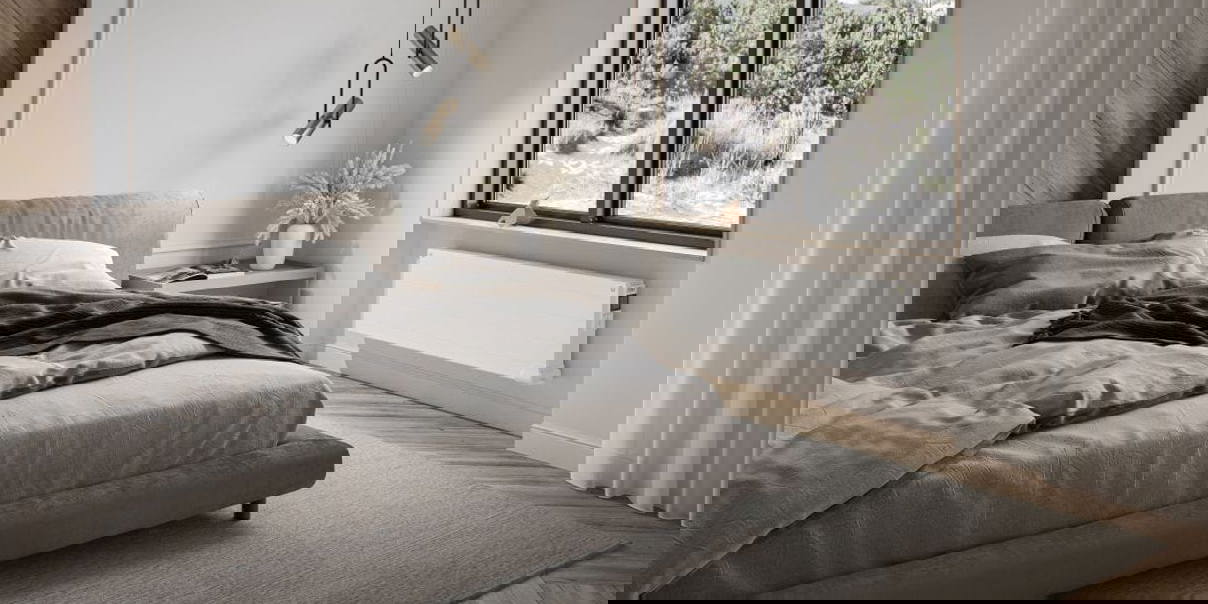 Modern bedroom interior with a sleek white radiator installed under a large window.