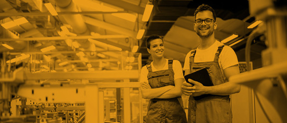 Two workers in a factory, smiling at the camera